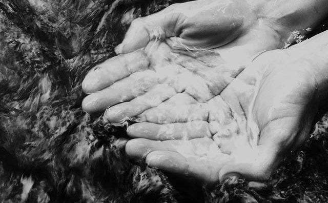 hands cupping water from clear running stream of water