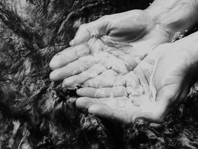 hands cupping water from clear running stream of water